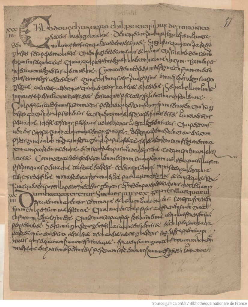 Page de parchemin manuscrite en écriture cursive mérovingienne, avec une grande lettrine ornée en début de page et une numérotation ancienne inscrite dans la marge.